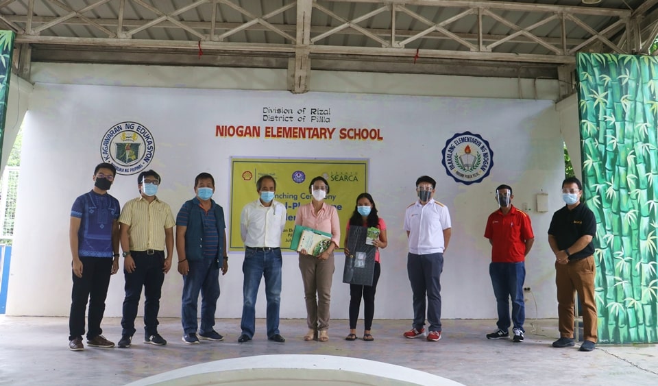 Ms. Jovelyn V. Ofianza (fourth from right), one of the parent beneficiaries, shows the gardening kit she received during the launching ceremony together with the SEARCA delegation comprised Mr. Nathan P. Felix (leftmost), Senior Public Relations Associate; Dr. Pedcris M. Orencio (second from left), Program Head for Research and Thought Leadership Department (RTLD); Mr. Manuel S. Alejar (fourth from left), Liaison for Community Relations; and Dr. Romeo V. Labios (rightmost), Operations Consultant for Partnerships; the PSFI delegation comprised Mr. Bernardo S. Camano, Jr. (second from right) and Mr. Pajee Ferc J. Salcedo (third from right); Mr. Onofre Benevidez (third from right), Chairman of Barangay Niogan; and Ms. Solita F. Combis, Niogan Elementary School Principal.