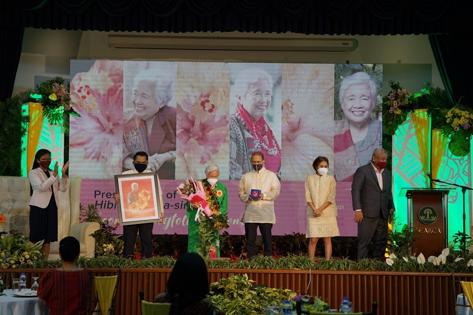 The H. rosa-sinensis ‘Leonor Magtolis Briones’ to Philippine Education Secretary Leonor Magtolis Briones (center) was presented by members of the UPLB community led by Plant Breeder Agripina O. Rasco (second from right), UPLB Institute of Plant Breeding. A portrait bearing a montage of the Secretary and the gumamela was presented by Dr. Jose V. Camacho, Jr. (second from left), UPLB Chancellor. A gumamela enamel brooch was pinned by Dr. Merdelyn C. Lit, UPLB Vice Chancellor for Research and Extension and Chair of the Committee on Naming of Hibiscus, Mussaenda and Other Ornamentals. A bouquet of the gumamela hybrid was given by Dr. Elpidio M. Agbisit, Jr., UPLB College of Agriculture and Food Sciences Dean. A paper weight bearing the gumamela montage was presented by Dr. Glenn B. Gregorio, SEARCA Director.